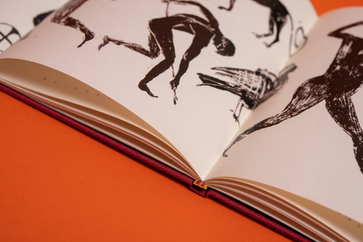 Libro abierto sobre fondo naranja: figuras dibujadas a tinta y la costura a mano con hilo naranja en el lomo